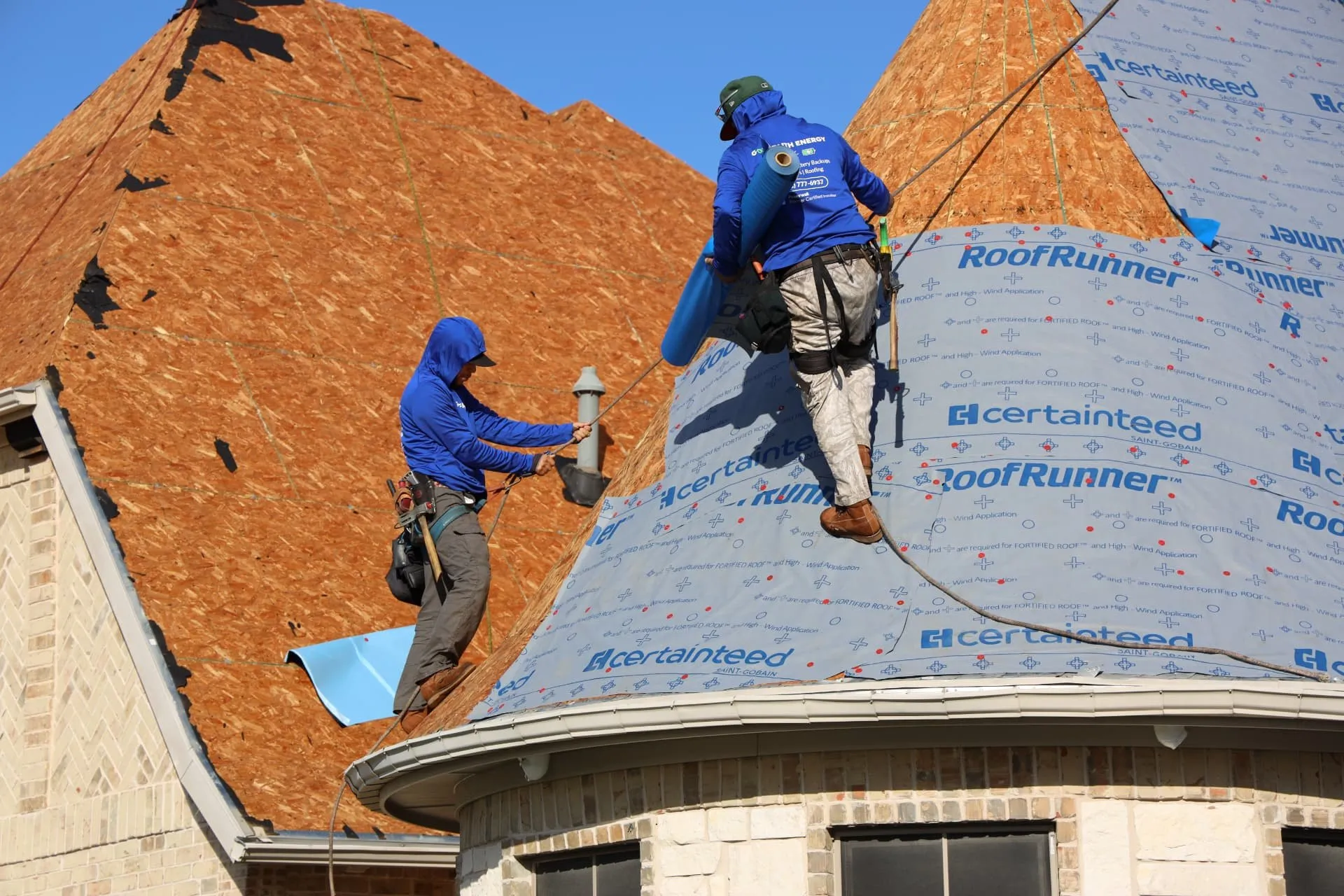 Roofing crew carrying a roll of synthetic underlayment onto the Prosper home's turret