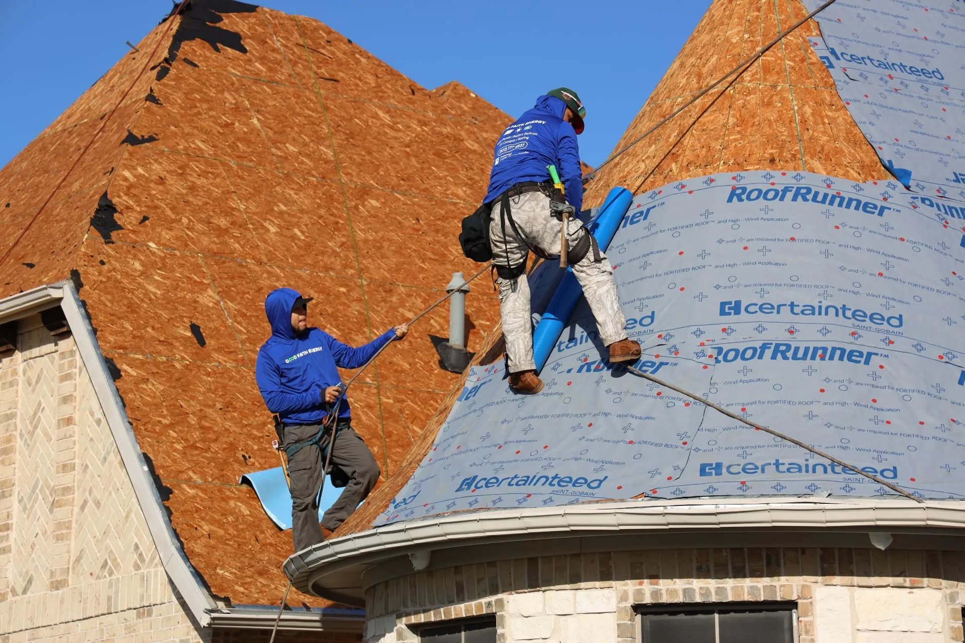 Two roofing installers working together on the Prosper turret roof during underlayment installation