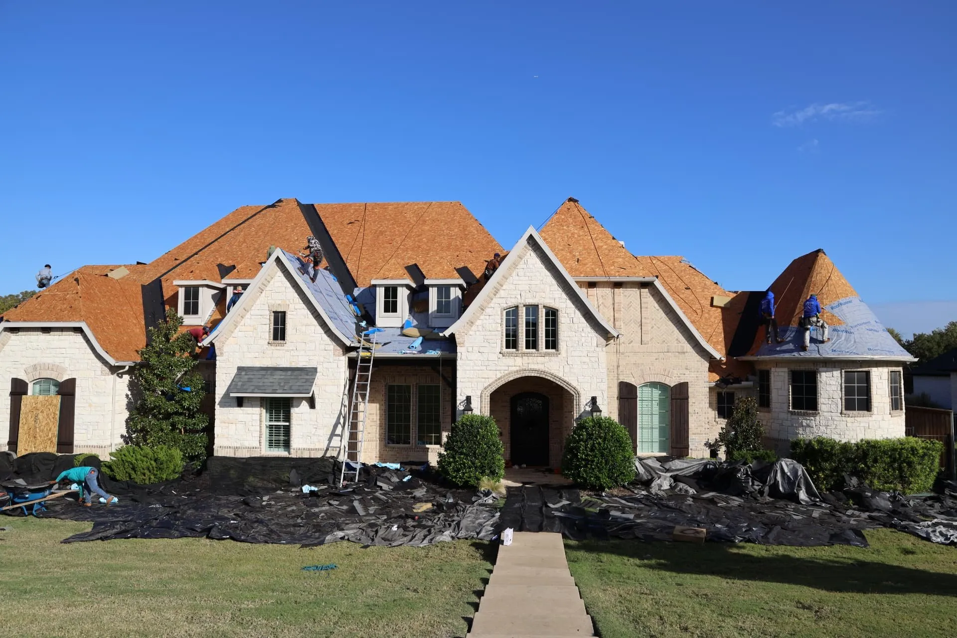Front of the Prosper home with crews preparing the roof and protective tarps across the landscaping