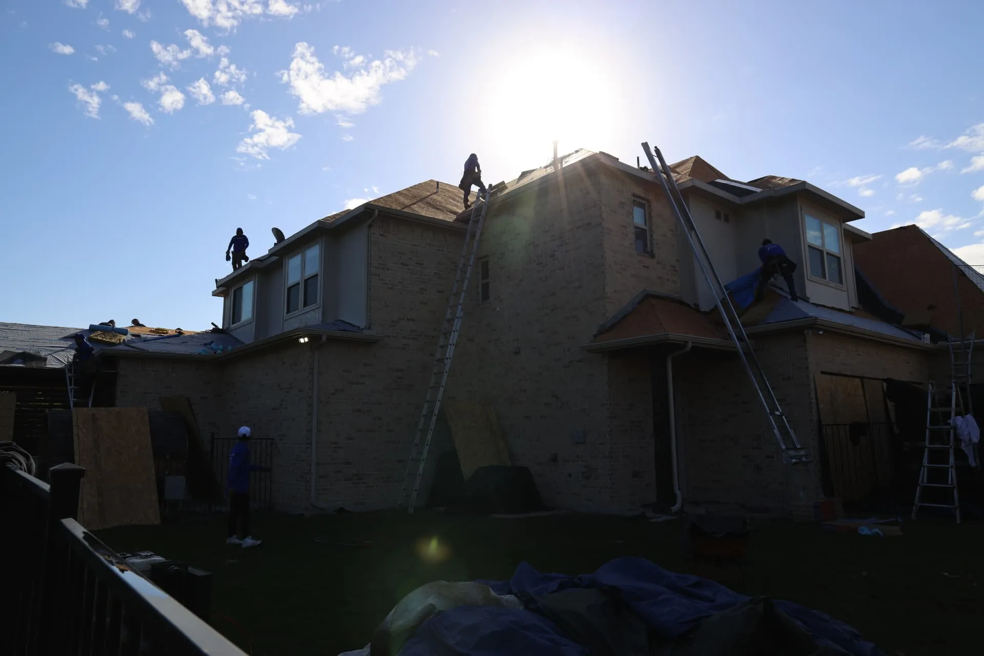 Backlit view of crew working on the rear roof slopes of the Prosper home