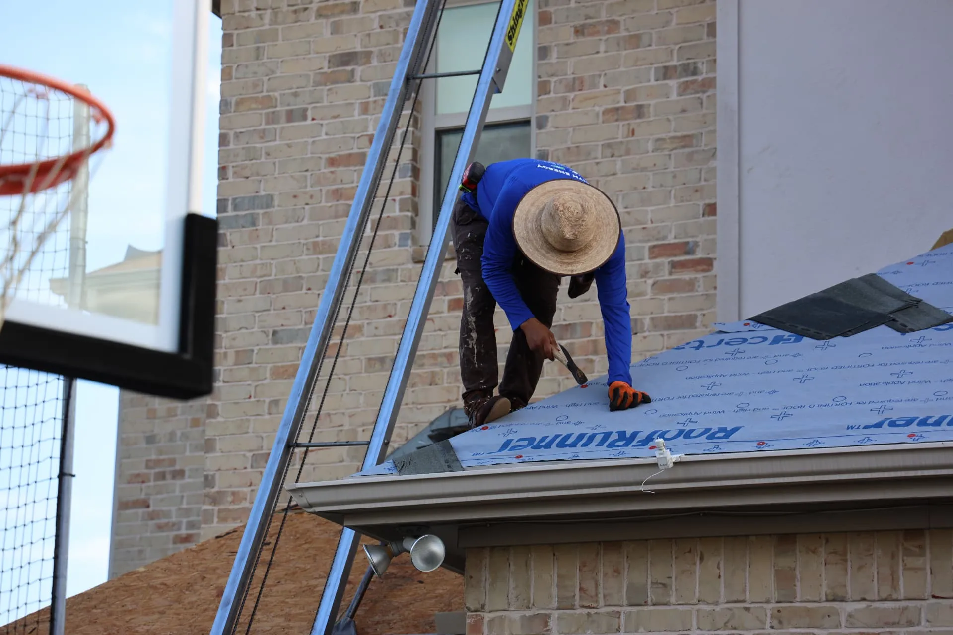 Installer securing synthetic underlayment beside a stone wall on the Prosper roof