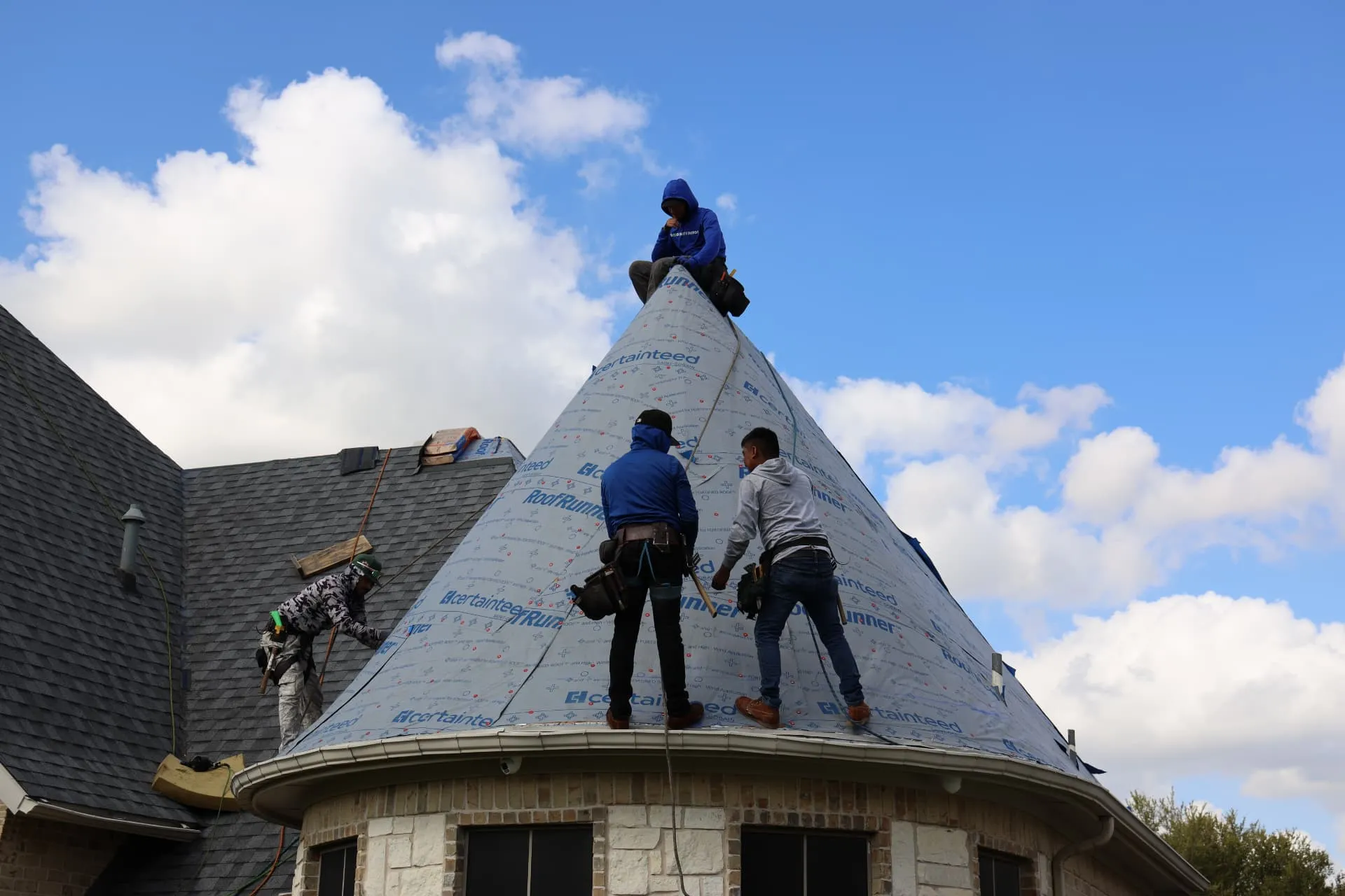 Roofing crew installing underlayment on the round turret roof of the Prosper home