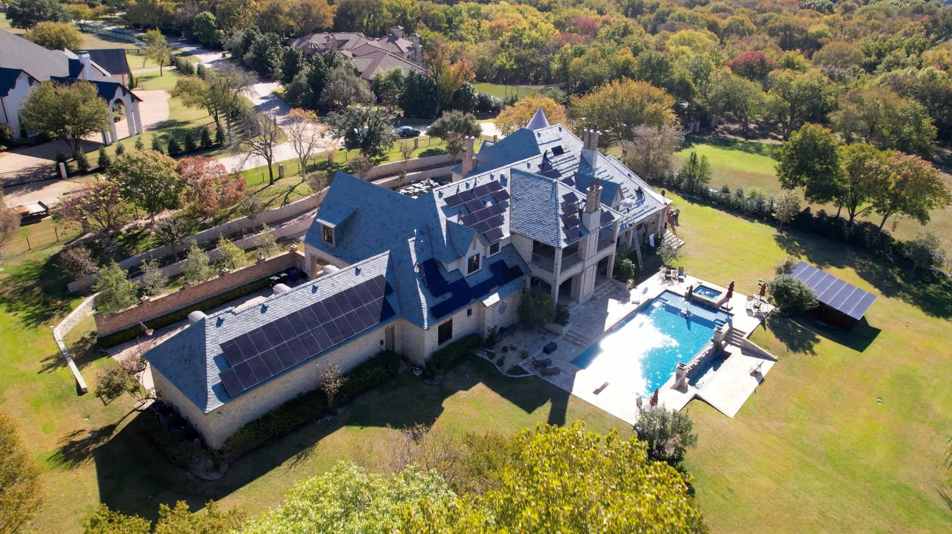 Aerial view of a Dallas-Fort Worth stone estate with a newly installed slate roof and rooftop solar panels