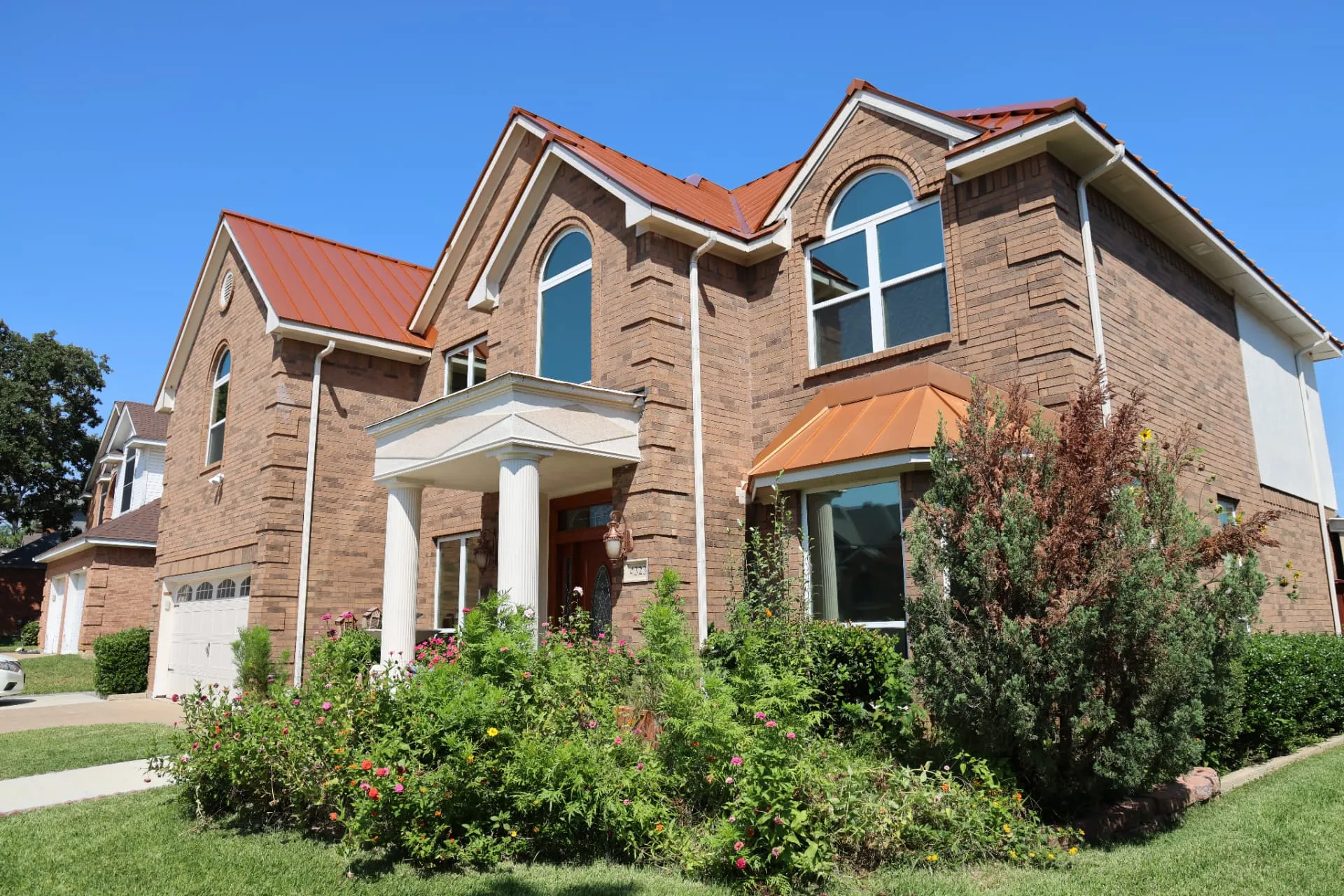Copper standing seam metal roof on a brick home seen from the front yard