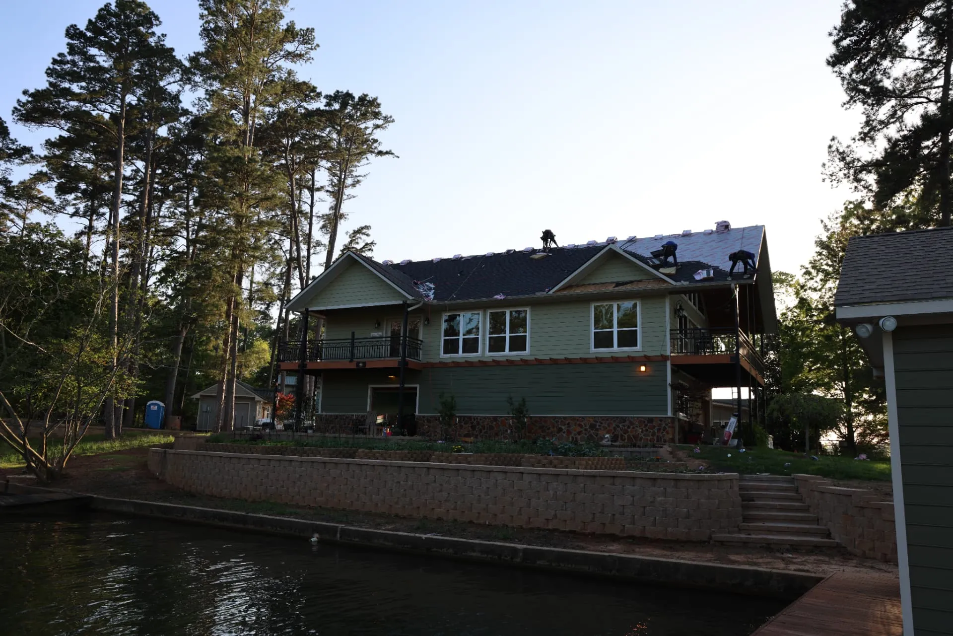 Good Faith Roofing crew installing new shingles on a storm-damaged lake house roof