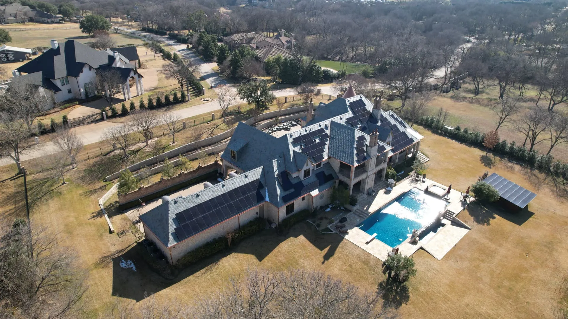 Aerial drone view of a DFW estate with roof-mounted solar panels during a coordinated roof replacement
